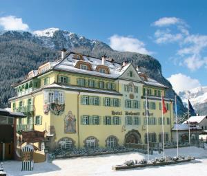 a large white building with a mountain range behind it at Hotel Dolomiti Schloss in Canazei