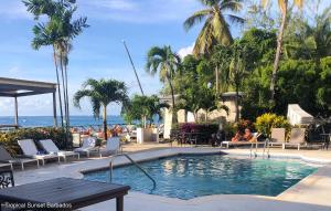 a swimming pool with chairs and a table and the ocean at Tropical Sunset Beach Apartment Hotel in Saint James