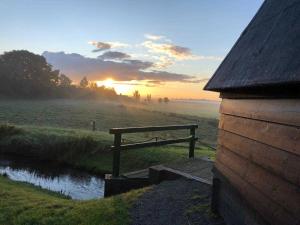een zonsondergang boven een veld met een houten bank naast een rivier bij Ferienhaus Kaept n Poldi 25192 in Bunde