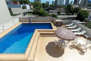 einen Pool mit einem Sonnenschirm und Stühlen sowie einem Tisch und einem Sonnenschirm in der Unterkunft Hotel Baviera Iguassu in Foz do Iguaçu