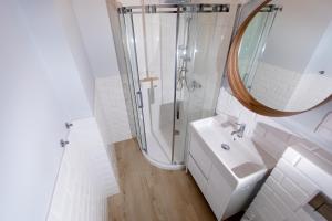 uma casa de banho branca com um chuveiro e um lavatório. em Apartamenty Pomona em Niechorze
