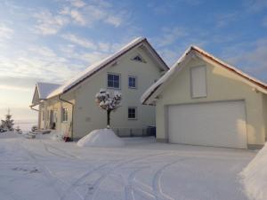 a white house with a garage in the snow at Ferienwohnung Vogelsang in Herdwangen-Schönach