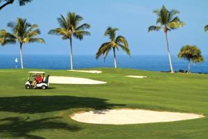 a man driving a golf cart on a golf course at Holua Resort in Kailua-Kona