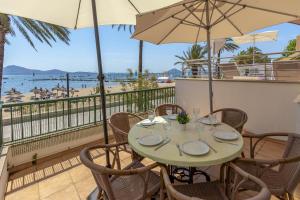 a table with chairs and an umbrella on a balcony with a beach at Apartamento DANIELA in Port de Pollensa