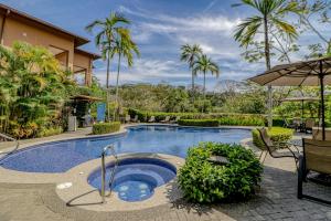 a swimming pool with an umbrella and palm trees at Veranda 5B in Herradura