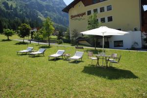 um grupo de cadeiras e uma mesa com um guarda-chuva em Pension Steinkogel em Sankt Leonhard im Pitztal