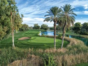 a golf course with palm trees and a pond at Orange Tree Resort in Scottsdale