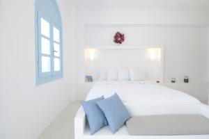 a white bedroom with a white bed with blue pillows at Villa Maria Rooms in Akrotiri