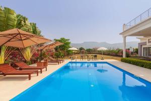 a swimming pool with chairs and umbrellas on a resort at Casa Del Vento by StayVista - Villa showcasing a swimming pool, Terrace with deck & A lush lawn with a gazebo for a delightful stay in Lonavala