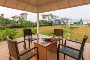 a patio with three chairs and a table with an umbrella at Casa Del Vento by StayVista - Villa showcasing a swimming pool, Terrace with deck & A lush lawn with a gazebo for a delightful stay in Lonavala