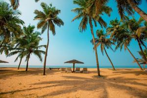 a beach with palm trees and a table and chairs at Malabar Ocean Front Resort And Spa, Bekal in Nīleshwar