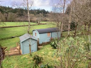 una pequeña casa azul en un campo con árboles en The Lookout Shepherd's Hut, en Dolton