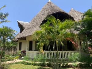 a house with a thatched roof and palm trees at Villa Twiga in Ukunda