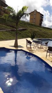 una piscina con sillas, una mesa y una palmera en Apartamento Condomínio Sonhos da Serra - Bananeiras, en Bananeiras