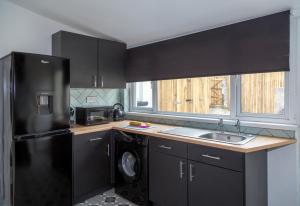 eine Küche mit schwarzen Schränken und einem schwarzen Kühlschrank in der Unterkunft Family friendly, Modern House just 1m from Bike Park Wales in Merthyr Tydfil