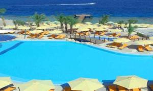 una piscina con sombrillas y sillas y el océano en Xperience Sea Breeze Resort, en Sharm El Sheikh