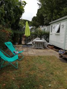 a yard with two chairs and a table and a umbrella at Mobilhome Oléron simple et spacieux à 1min de l'Océan in La Cotinière