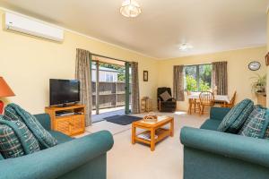 uma sala de estar com dois sofás azuis e uma televisão em Hibiscus House - Mangawhai Heads Holiday Home em Mangawhai