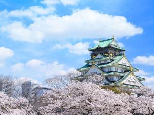 a large building with a clock tower behindakura trees at HOTEL HILLARYS Shinsaibashi in Osaka