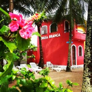 a red building with chairs and palm trees in front of it at Pousada Coruja Branca in Berlinque