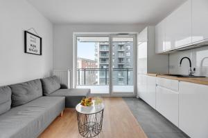 a living room with a gray couch and a kitchen at Apartament Bastion Sky Gdańsk TriApart in Gdańsk