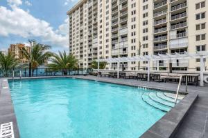 a large pool with tables and umbrellas in front of buildings at Cambria Hotel Fort Lauderdale Beach in Fort Lauderdale