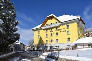 un edificio giallo con neve per terra di Hotel Vittoria a Folgaria