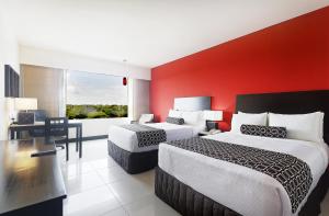 Crowne Plaza Villahermosa, an IHG Hotel في فيلاهيرموسا: غرفة فندقية بسريرين وجدار احمر