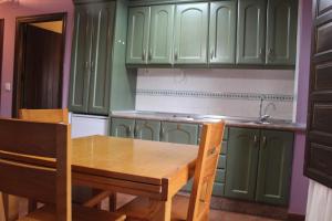 a kitchen with green cabinets and a wooden table and chairs at Apartamentos NOGUERA de ALBARRACÍN in Noguera de Albarracin