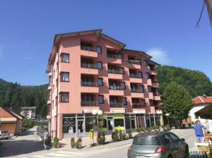 a large pink building with cars parked in front of it at Apartman Gold City 2 Studio in Fojnica