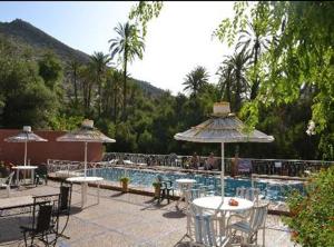 伊莫采德艾達塔納内的住宿－Maison d'hôtes tifrit-Paradise valley，游泳池配有桌子和遮阳伞,周围的人坐在游泳池周围