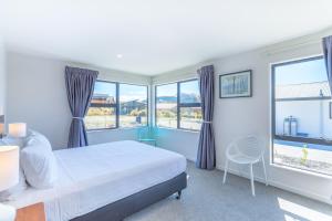 a bedroom with a bed and two windows and a chair at Neptune - Lake Tekapo in Lake Tekapo