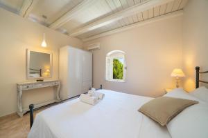 a white bedroom with a large white bed and a window at Blue Horizon Cottages in Tzamarelláta