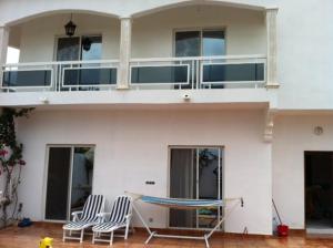 une maison blanche avec deux chaises et un hamac devant elle dans l'établissement Villa à Thiès avec piscine à 15mn de l'aéroport, à Thiès
