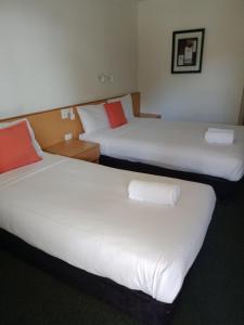 Cette chambre comprend 2 lits avec des draps blancs et des oreillers rouges. dans l'établissement Annerley Motor Inn, à Brisbane
