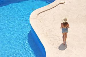 a woman in a hat walking along a swimming pool at Aparthotel Niu d´Aus in Portopetro