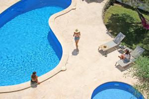 a woman in a hat is standing next to a swimming pool at Aparthotel Niu d´Aus in Portopetro