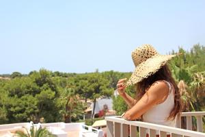 a woman wearing a straw hat sitting on a balcony at Aparthotel Niu d´Aus in Portopetro