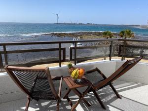 a table with a bowl of fruit and a chair on a balcony overlooking the beach at Arinaga Colors, tu casa en la playa in Arinaga