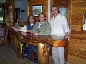 un hombre y dos mujeres parados junto a un mostrador de madera en Hosteria Al Paraiso en Villa Pehuenia