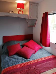 Una cama con almohadas rojas en una habitación pequeña. en Le pré vert, en Campigny