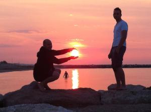 two men standing on rocks on the beach at sunset at Hotel Berna in Eraclea Mare