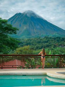 una mujer en bikini sentada en una valla con vistas a una montaña en Miradas Arenal Hotel & Hotsprings, en Fortuna