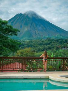 a woman in a bikini sitting on a fence overlooking a mountain at Miradas Arenal Hotel & Hotsprings in Fortuna