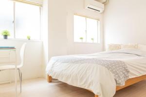 a white bedroom with a bed and a desk and windows at Casa Blanca Guesthouse in Nagasaki