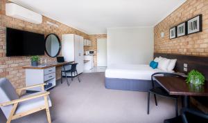 Sunshine Coast Motor Lodge في Woombye: غرفة في الفندق بها سرير ومكتب ومرآة