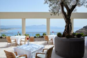 un restaurante con mesas y sillas blancas y un árbol en Lindos Blu Luxury Hotel-Adults only, en Lindos