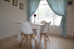 mesa de comedor con sillas blancas y ventana en The Open Door Guest Suite, en Modimolle