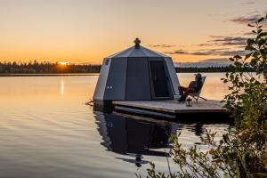 a person sitting on a dock next to a tent on a lake at Aurora Hut Savonlinna in Savonlinna