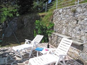 3 weiße Stühle und ein Tisch vor einer Steinmauer in der Unterkunft Holiday Home Villetta degli Orti by Interhome in Montemagno